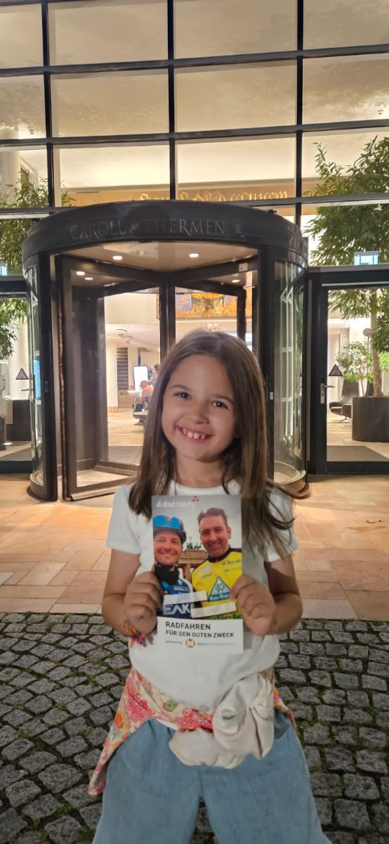 Die kleine Liv mit der all about charity Postkarte vor den Carolus Thermen